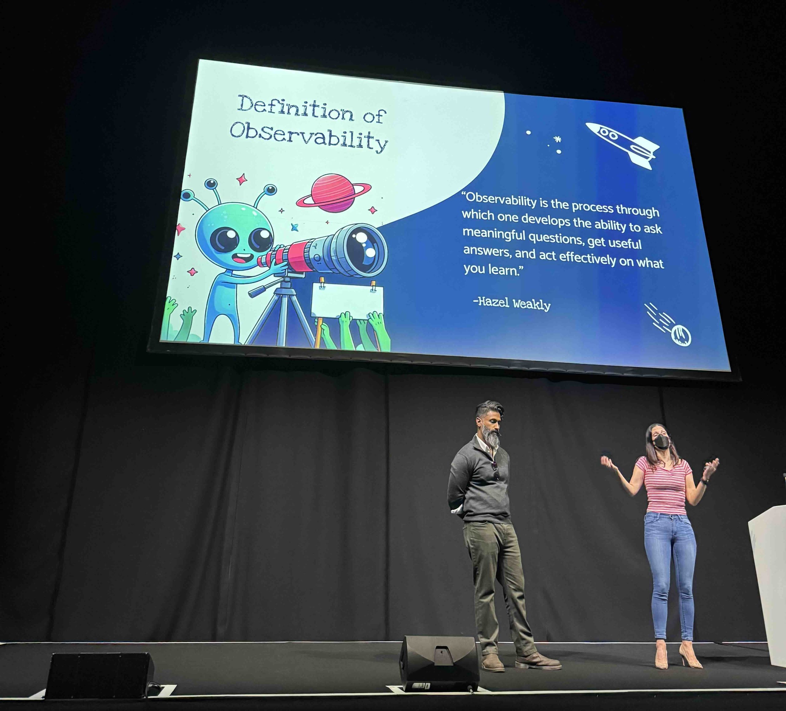 Adriana Villela and Marino Wijay on a stage presenting slides at KubeCon EU 2025